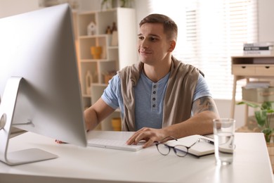 Handsome man working with computer at desk indoors. Home office