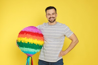 Photo of Happy man with colorful pinata on yellow background