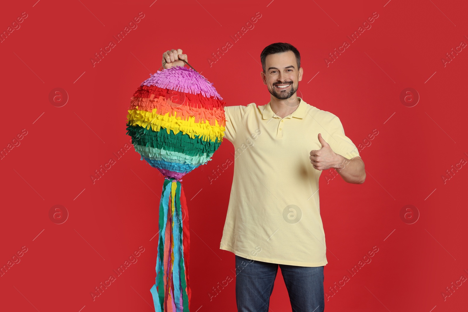 Photo of Happy man with colorful pinata showing thumbs up on red background