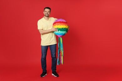 Photo of Happy man with colorful pinata on red background