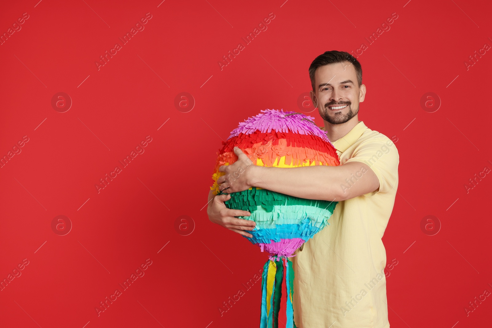 Photo of Happy man with colorful pinata on red background, space for text