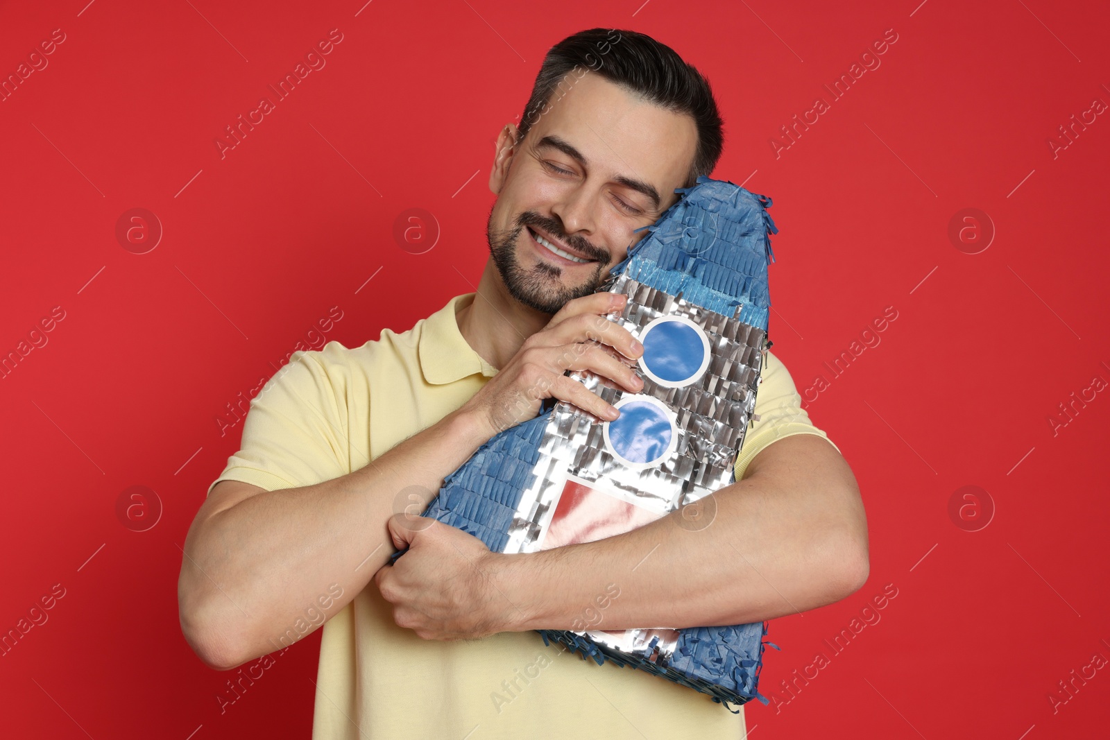 Photo of Happy man with rocket shaped pinata on red background