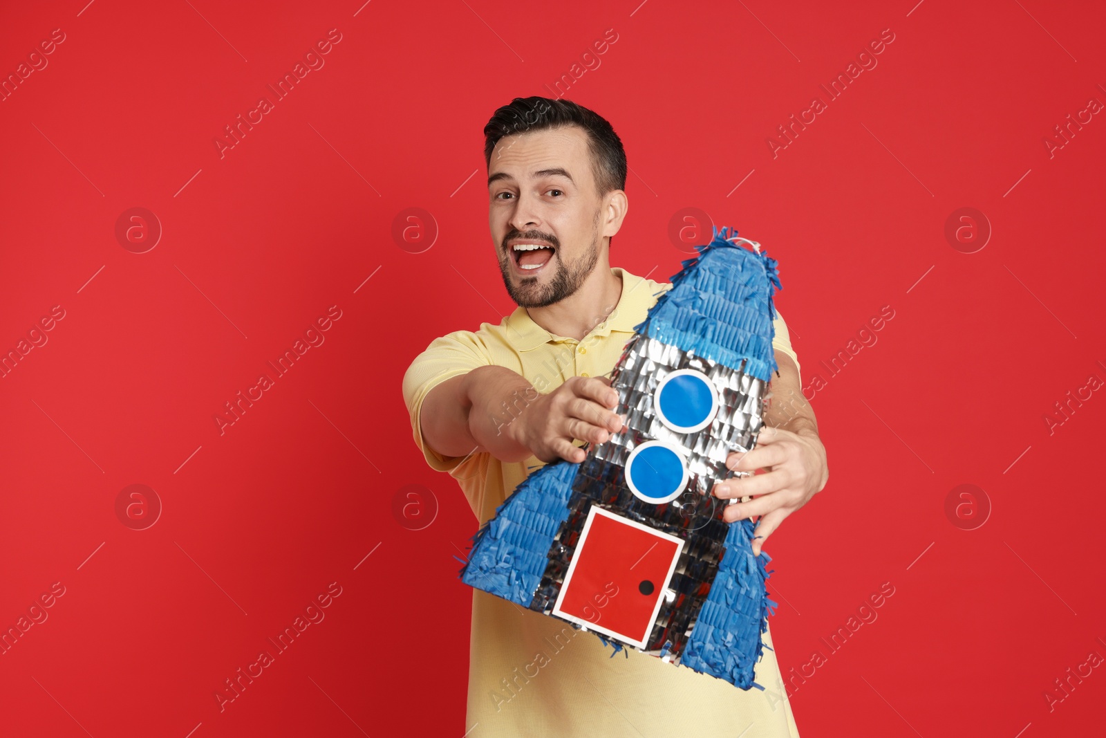 Photo of Happy man with rocket shaped pinata on red background