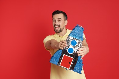 Photo of Happy man with rocket shaped pinata on red background