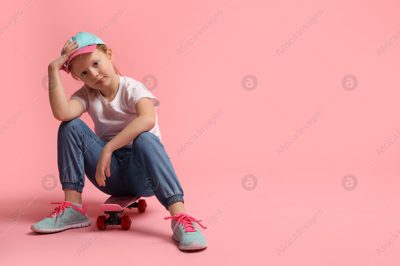 Photo of Little girl sitting on penny board against pink background, space for text