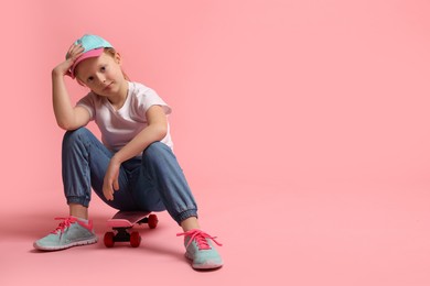 Photo of Little girl sitting on penny board against pink background, space for text