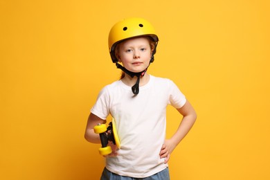 Little girl in helmet with penny board on orange background