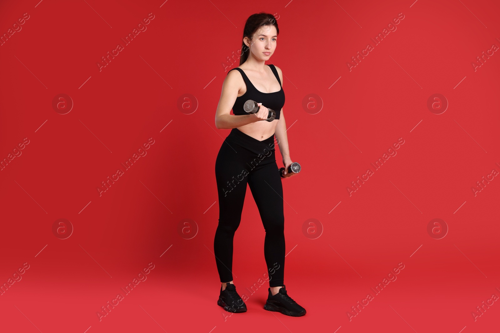 Photo of Woman in sportswear exercising with dumbbells on red background