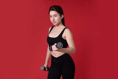 Woman in sportswear exercising with dumbbells on red background