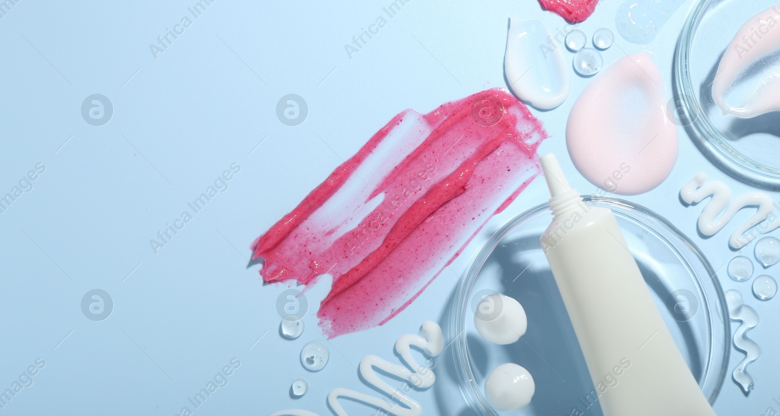 Photo of Cream, scrub and gel samples on light blue background, flat lay. Stylish presentation with tube of skincare product. Space for text