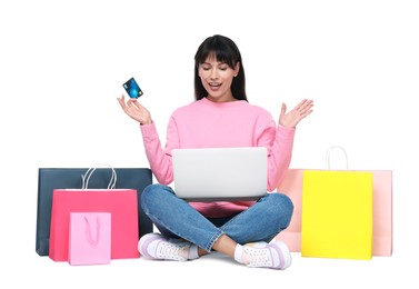 Photo of Internet shopping. Surprised woman with credit card, laptop and colorful bags on white background