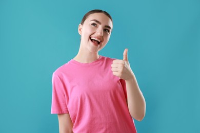 Photo of Happy woman showing thumbs up on light blue background. Like gesture