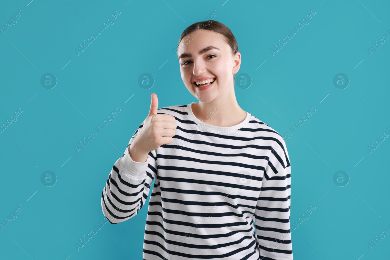 Photo of Happy woman showing thumbs up on light blue background. Like gesture