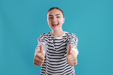 Photo of Happy woman showing thumbs up on light blue background. Like gesture