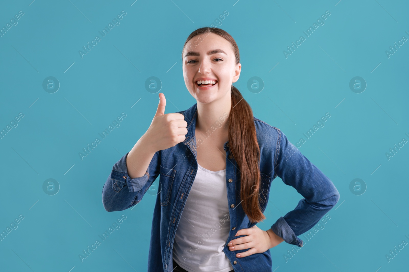 Photo of Happy woman showing thumbs up on light blue background. Like gesture