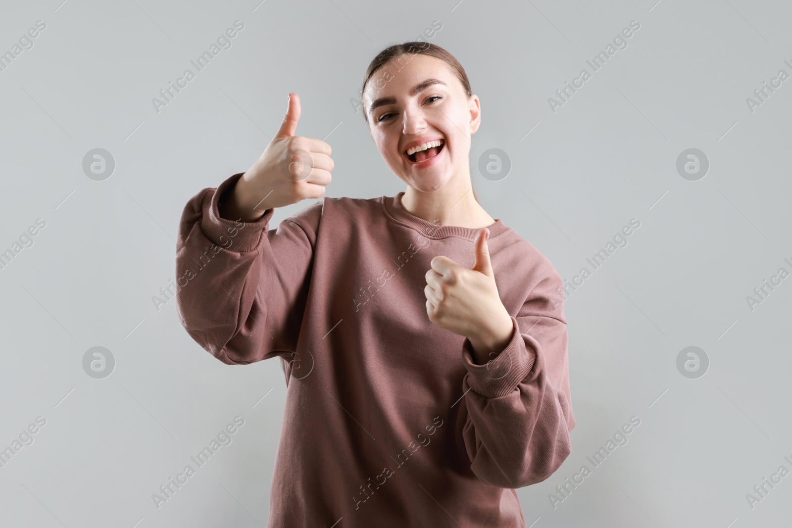 Photo of Happy woman showing thumbs up on grey background. Like gesture