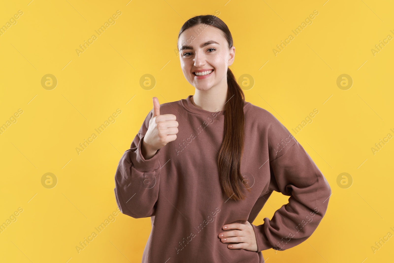 Photo of Happy woman showing thumbs up on yellow background. Like gesture