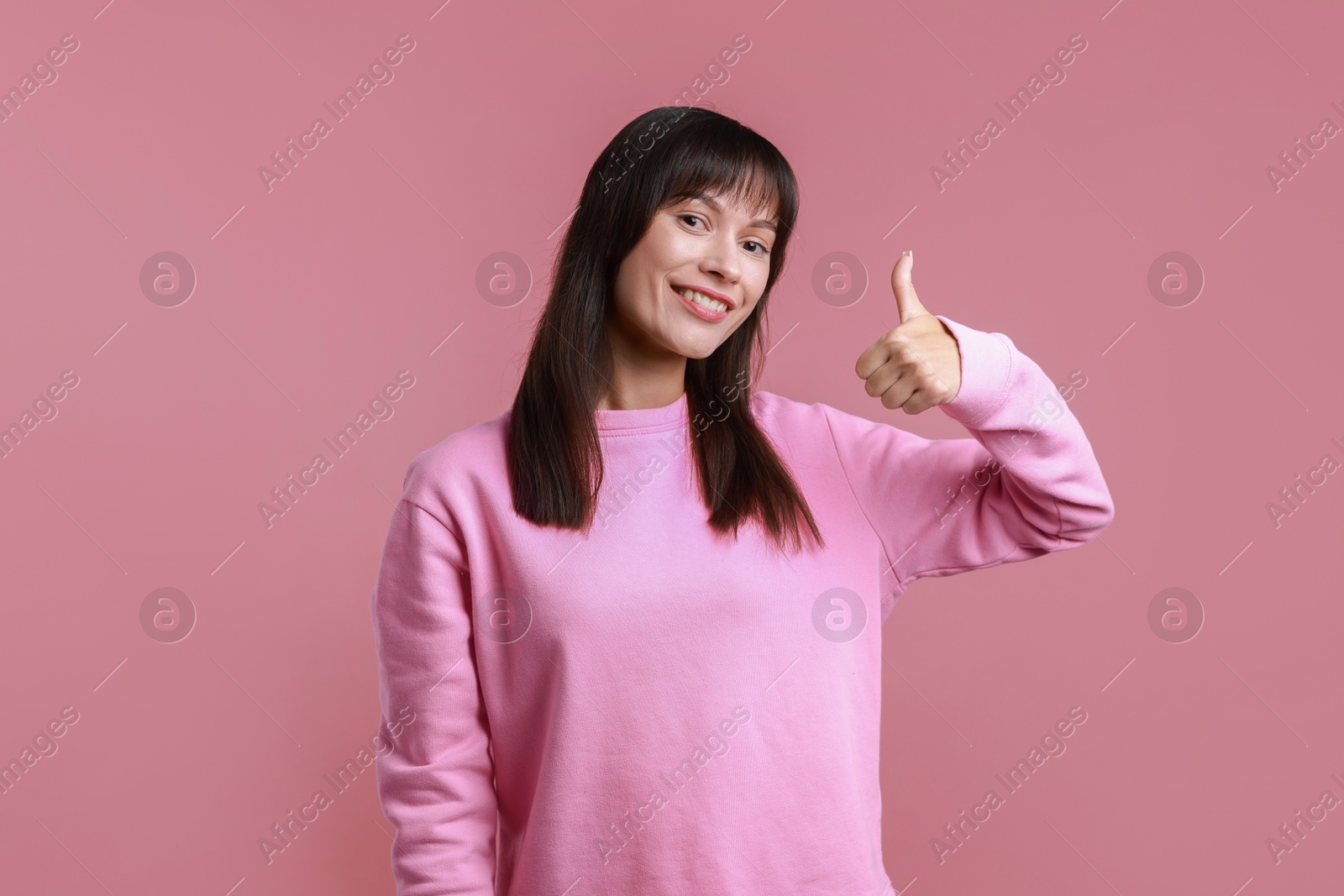 Photo of Happy woman showing thumbs up on pink background. Like gesture