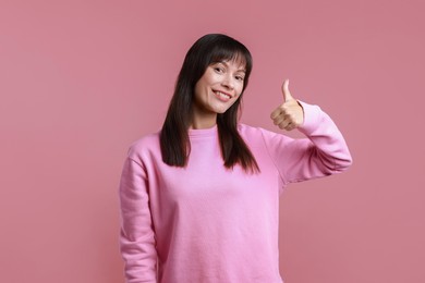 Happy woman showing thumbs up on pink background. Like gesture