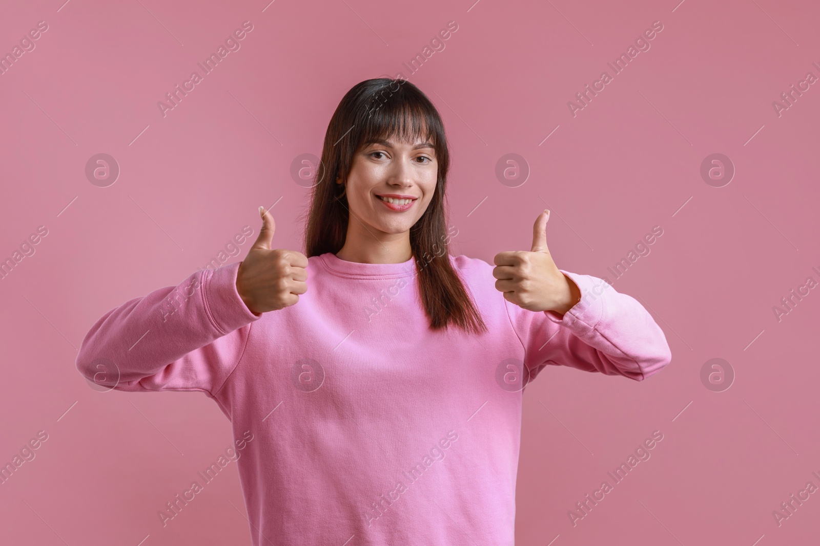 Photo of Happy woman showing thumbs up on pink background. Like gesture