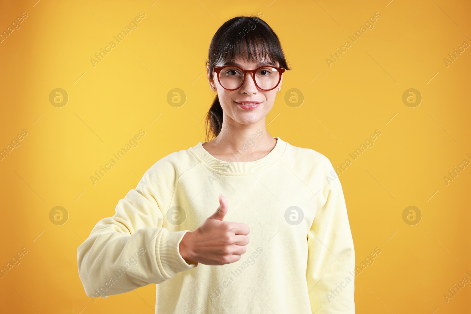 Photo of Happy woman showing thumbs up on orange background. Like gesture