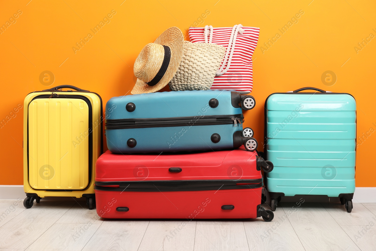 Photo of Many colorful suitcases, beach bags and hat on floor near orange wall