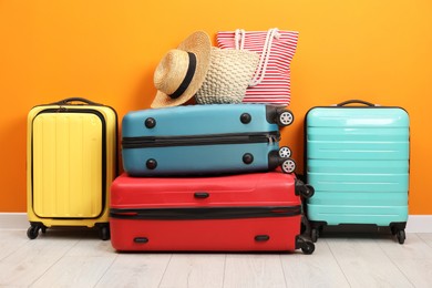 Photo of Many colorful suitcases, beach bags and hat on floor near orange wall