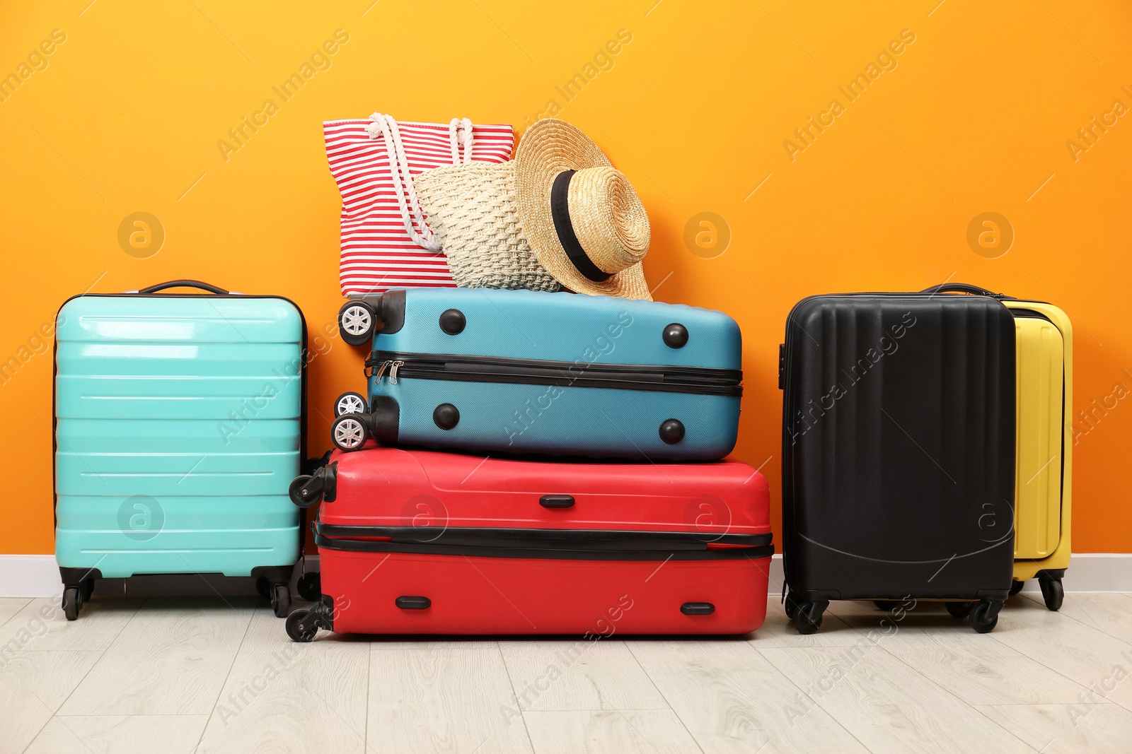 Photo of Many colorful suitcases, beach bags and hat on floor near orange wall