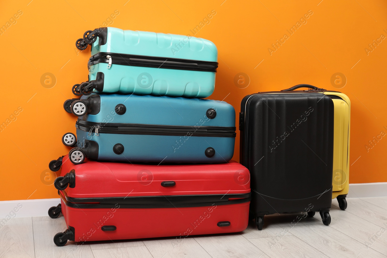 Photo of Many colorful suitcases on floor near orange wall