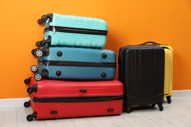 Many colorful suitcases on floor near orange wall