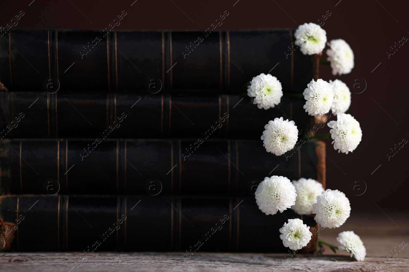 Photo of Stack of books with beautiful flowers on wooden table, closeup