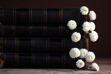 Stack of books with beautiful flowers on wooden table, closeup