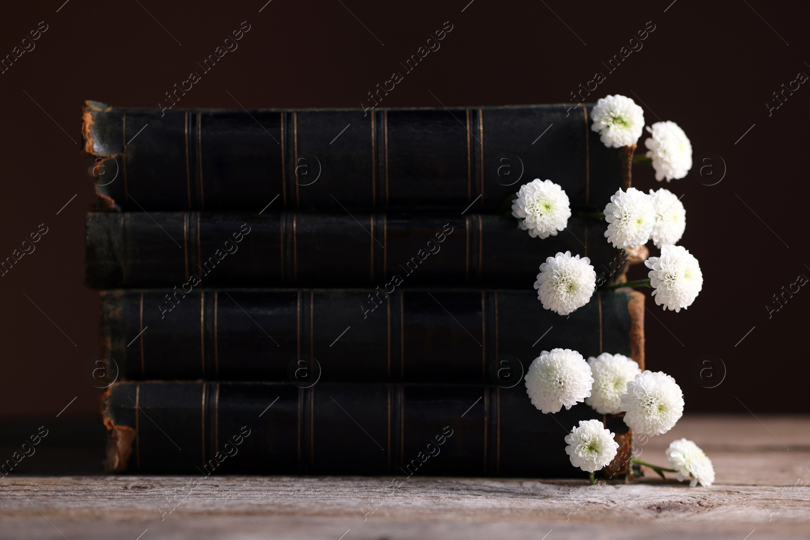 Photo of Stack of books with beautiful flowers on wooden table, closeup