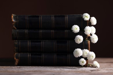 Stack of books with beautiful flowers on wooden table, closeup