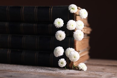 Photo of Stack of books with beautiful flowers on wooden table, closeup