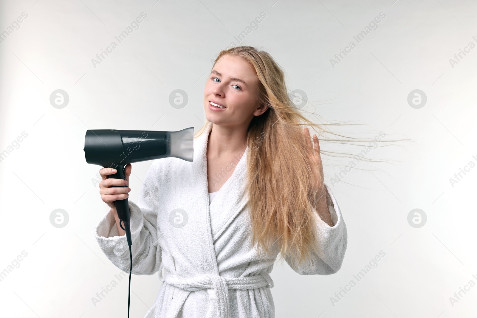 Photo of Beautiful young woman drying her hair with hairdryer on light grey background