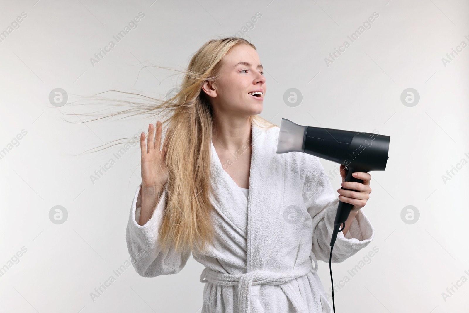 Photo of Beautiful young woman drying her hair with hairdryer on light grey background