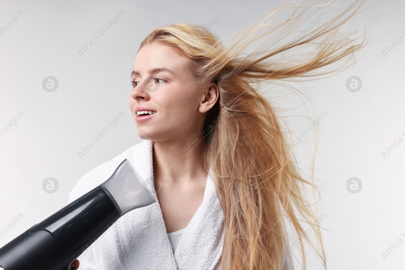 Photo of Beautiful young woman drying her hair with hairdryer on light grey background