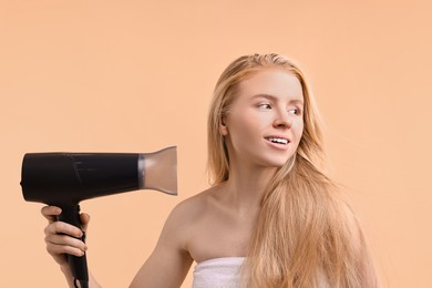 Photo of Beautiful young woman drying her hair with hairdryer on beige background