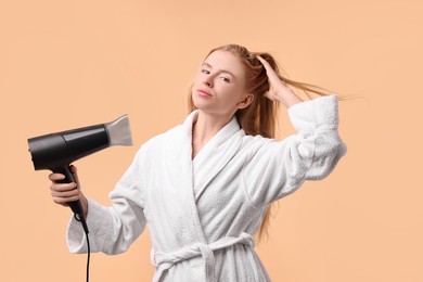 Photo of Beautiful young woman drying her hair with hairdryer on beige background