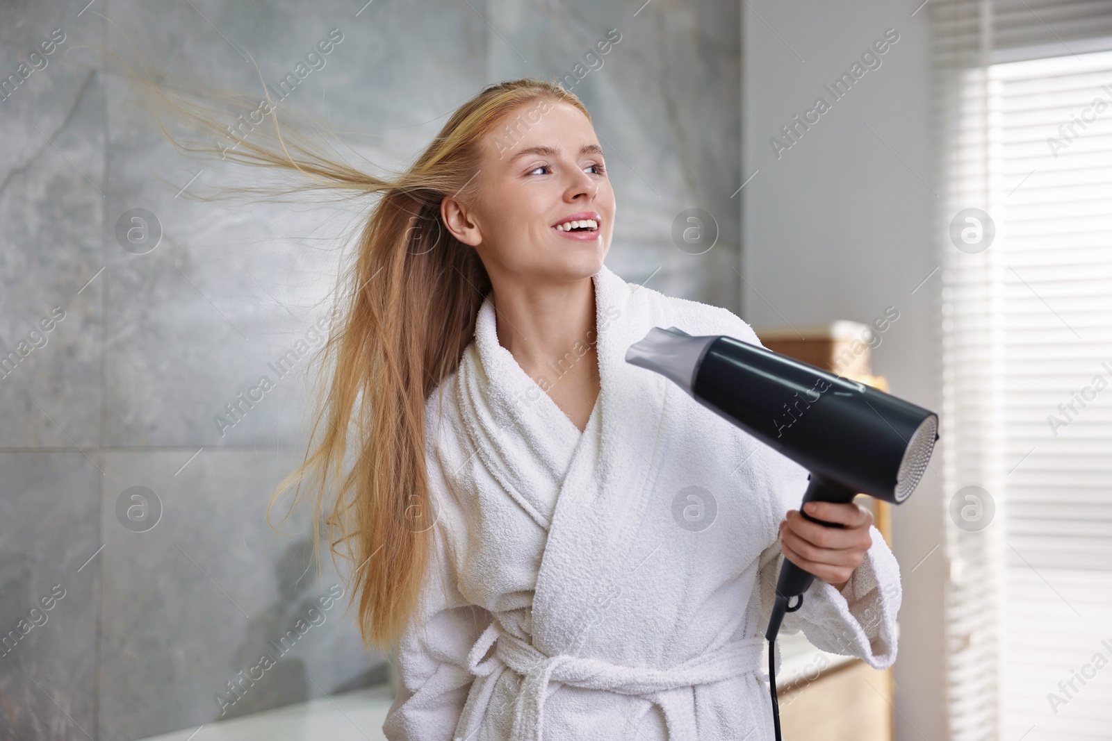 Photo of Beautiful young woman drying her hair in bathroom