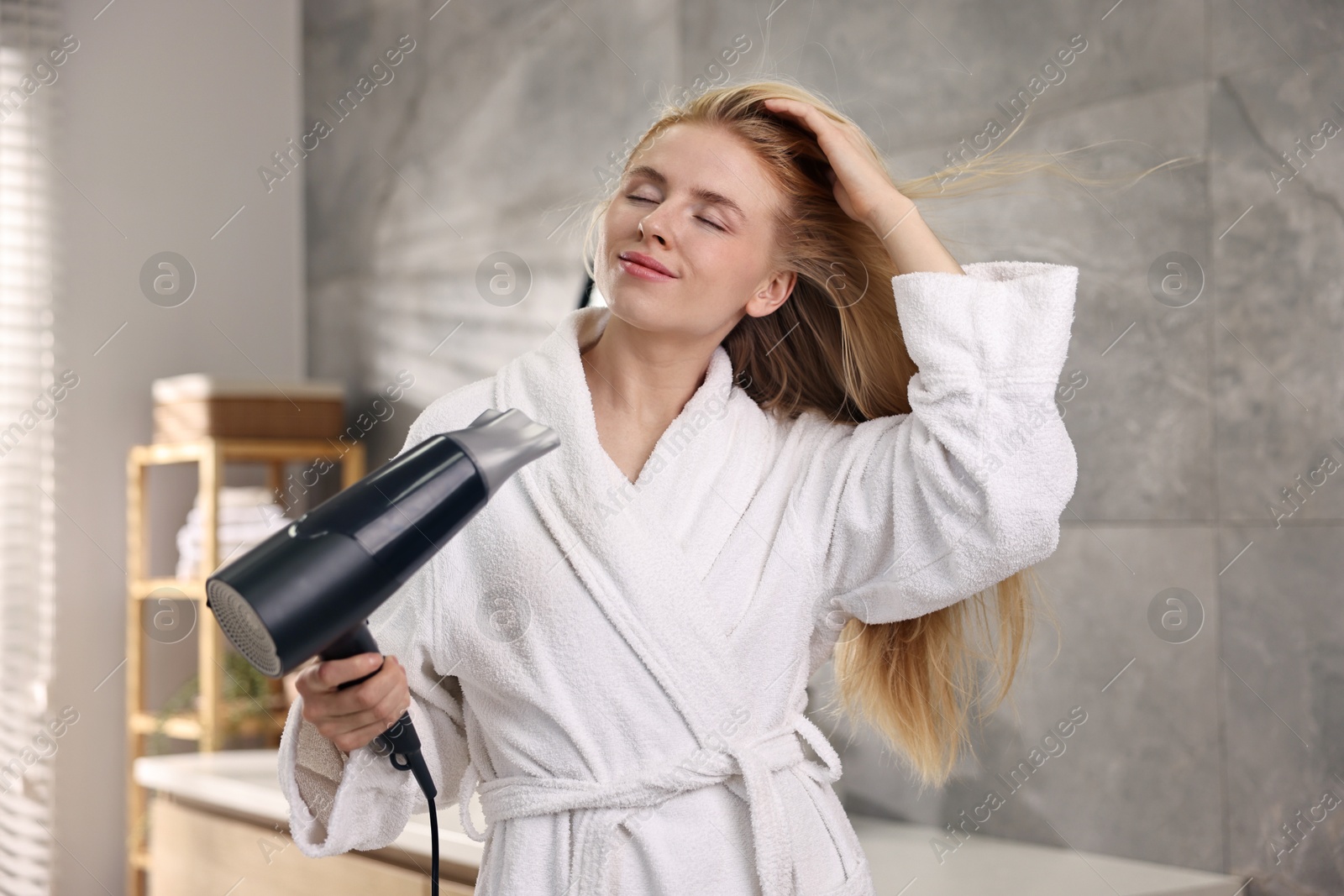 Photo of Beautiful young woman drying her hair in bathroom