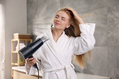 Beautiful young woman drying her hair in bathroom