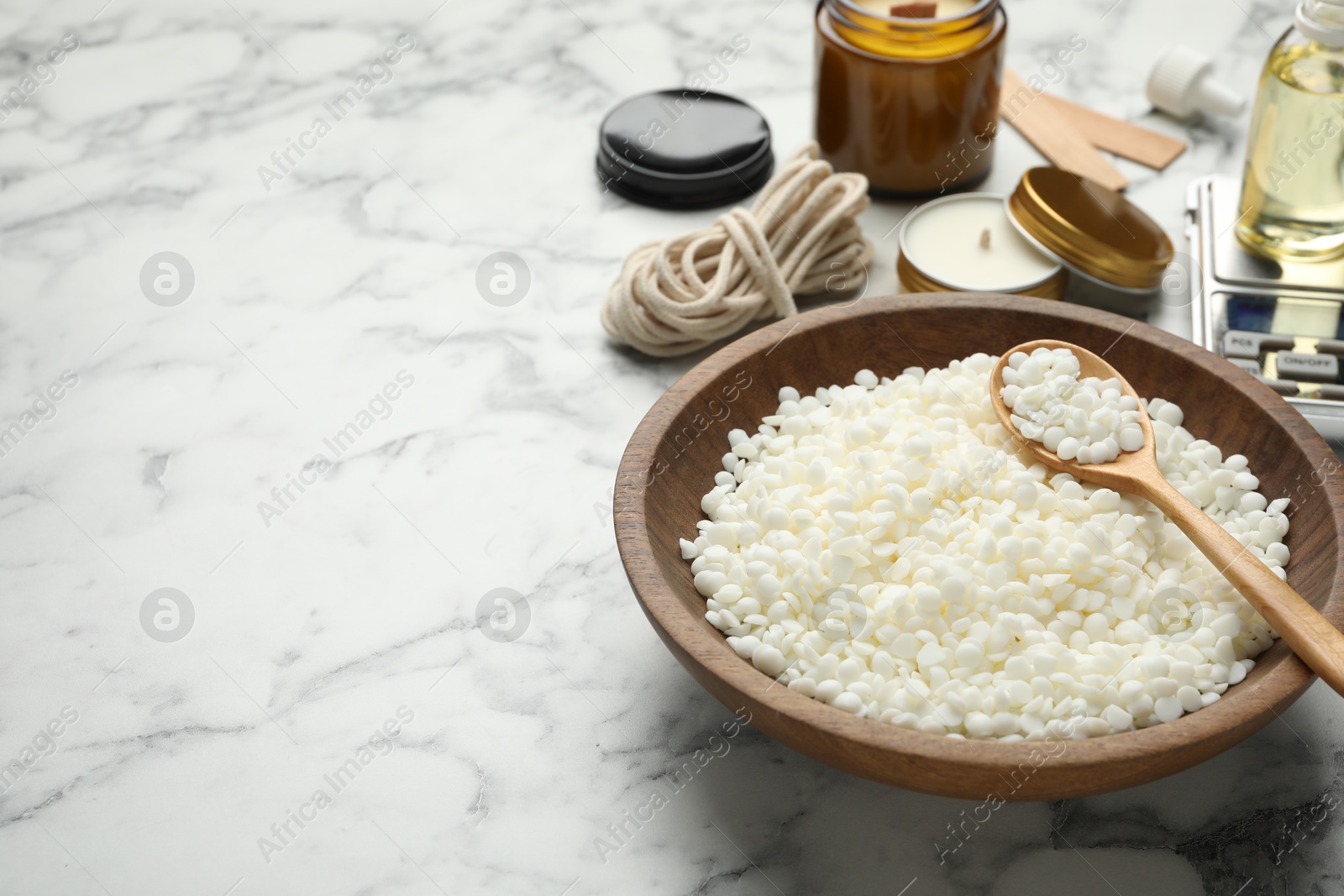 Photo of Soy wax and other supplies for making candles on white marble table, closeup. Space for text