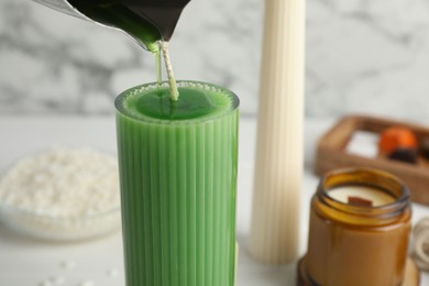 Photo of Making handmade candles. Pouring melted soy wax into glass mold on light table, closeup