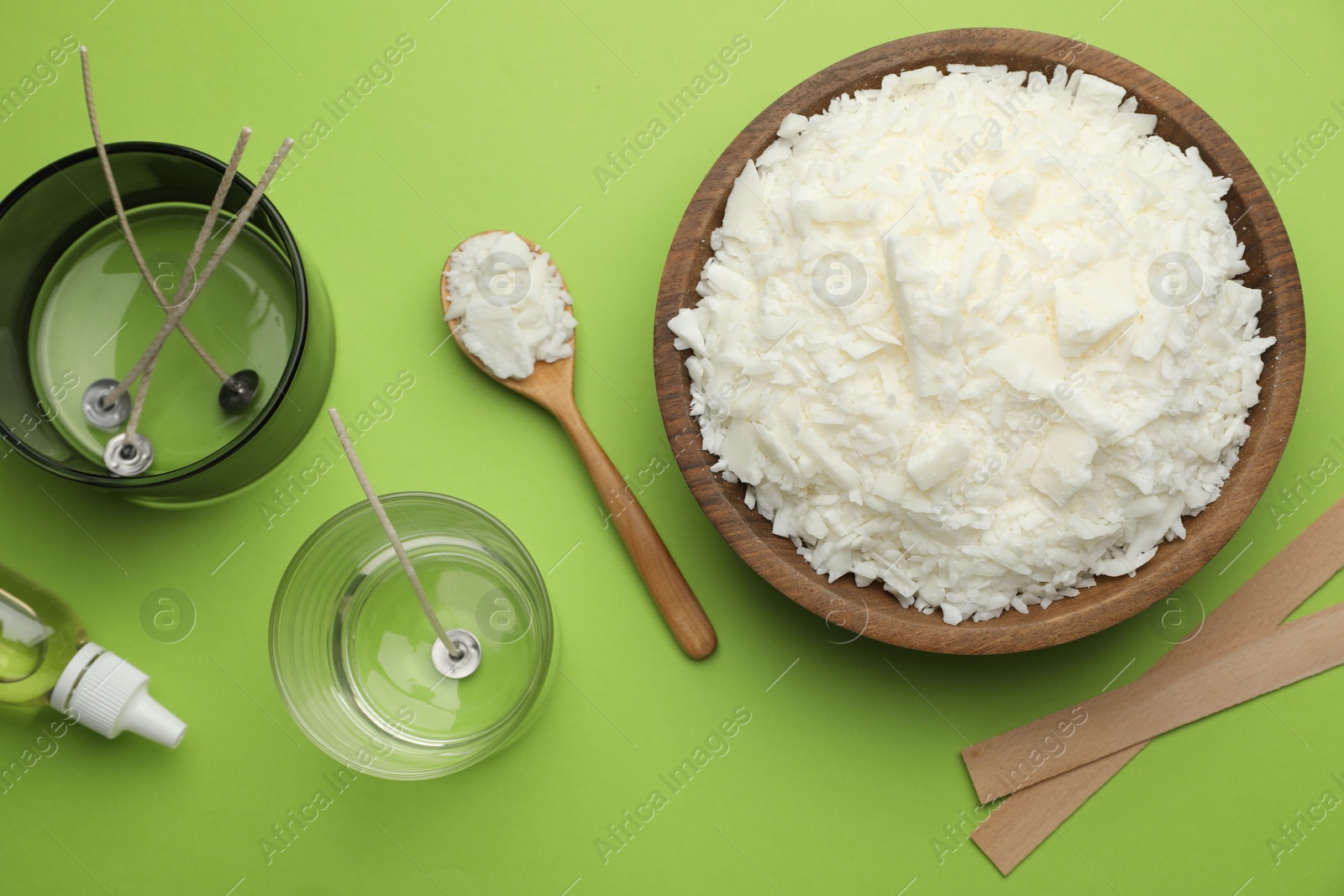 Photo of Making homemade candles. Soy wax in bowl, jars with stabilizers, wicks and essential oil on green background, flat lay