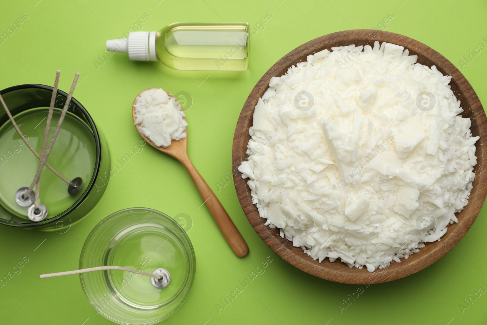 Photo of Making homemade candles. Soy wax in bowl, jars with stabilizers, wicks and essential oil on green background, flat lay