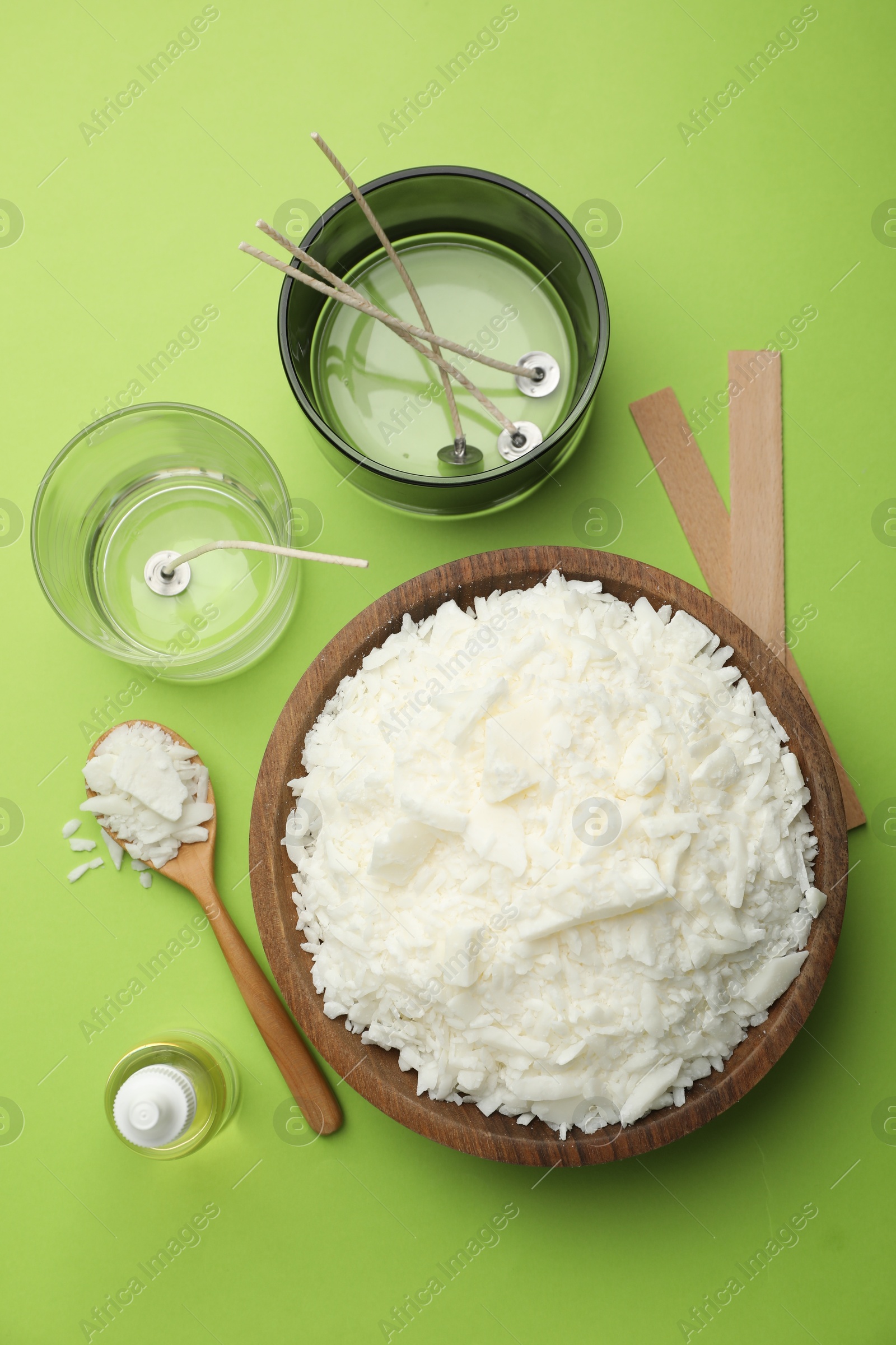 Photo of Making homemade candles. Soy wax in bowl, jars with stabilizers, wicks and essential oil on green background, flat lay