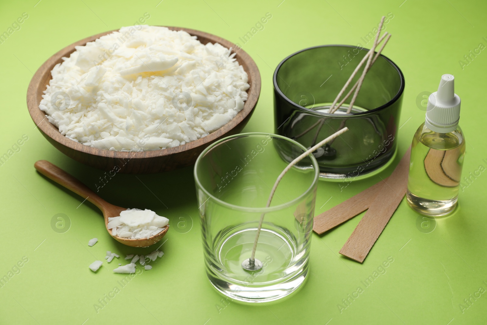 Photo of Making homemade candles. Soy wax in bowl, jars with stabilizers, wicks and essential oil on green background, closeup