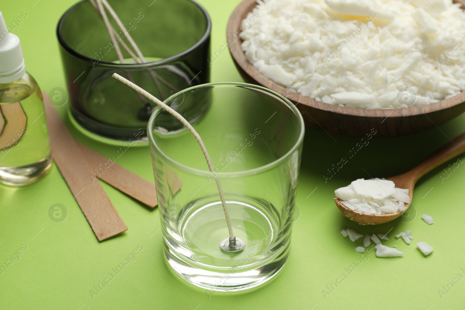 Photo of Making homemade candles. Soy wax in bowl, jars with stabilizers, wicks and essential oil on green background, closeup